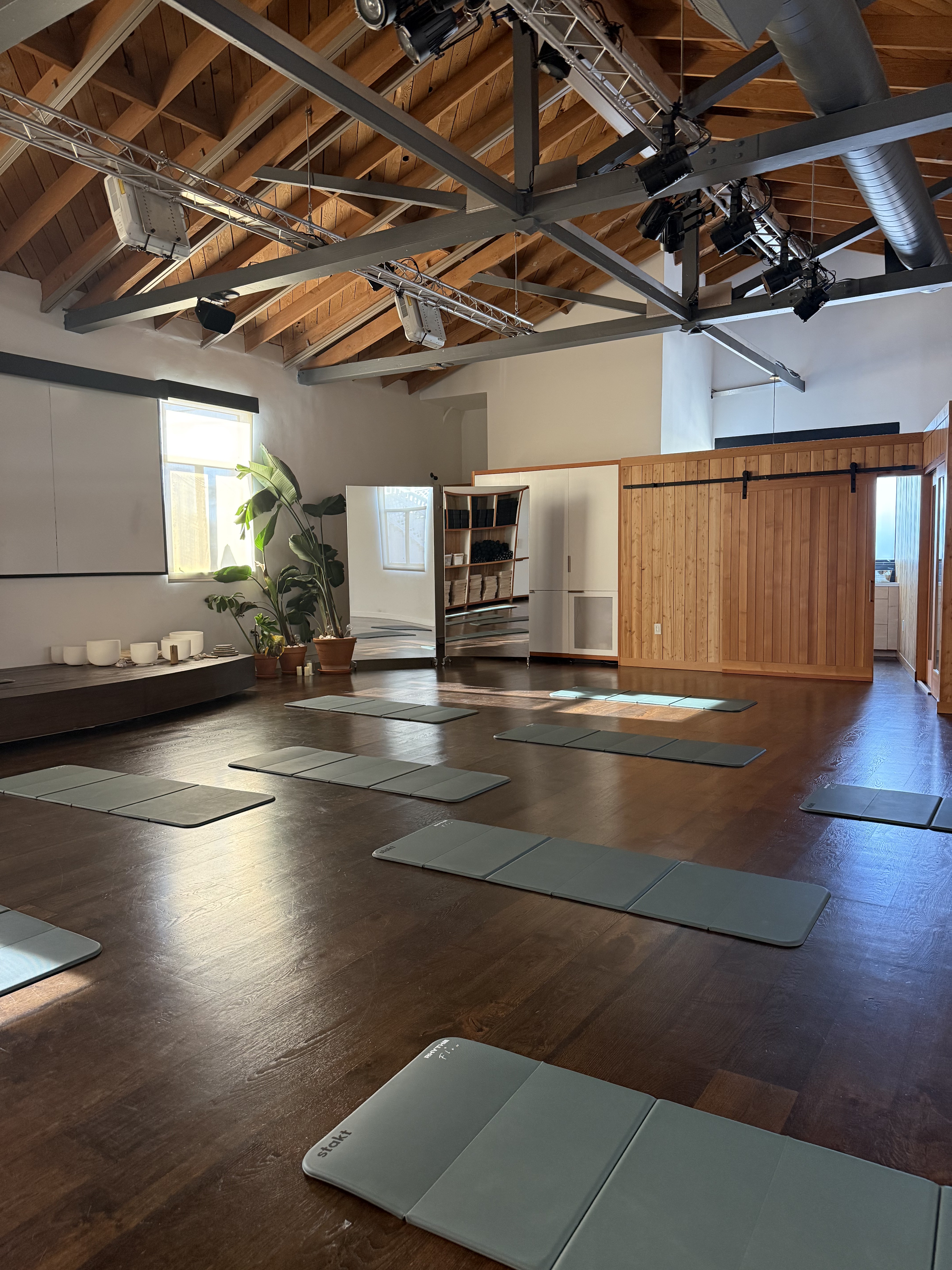Sunlit yoga and breathwork studio with wood beams, mats, and sound bowls
